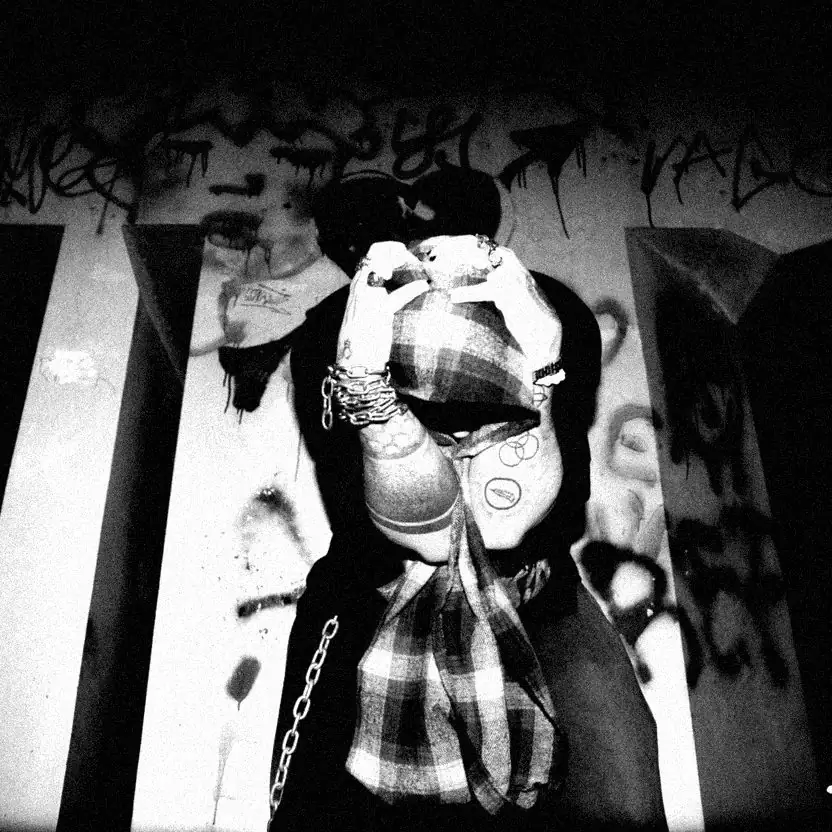 Cap Kuo contra una pared con graffiti, tapándose la cara con la camisa